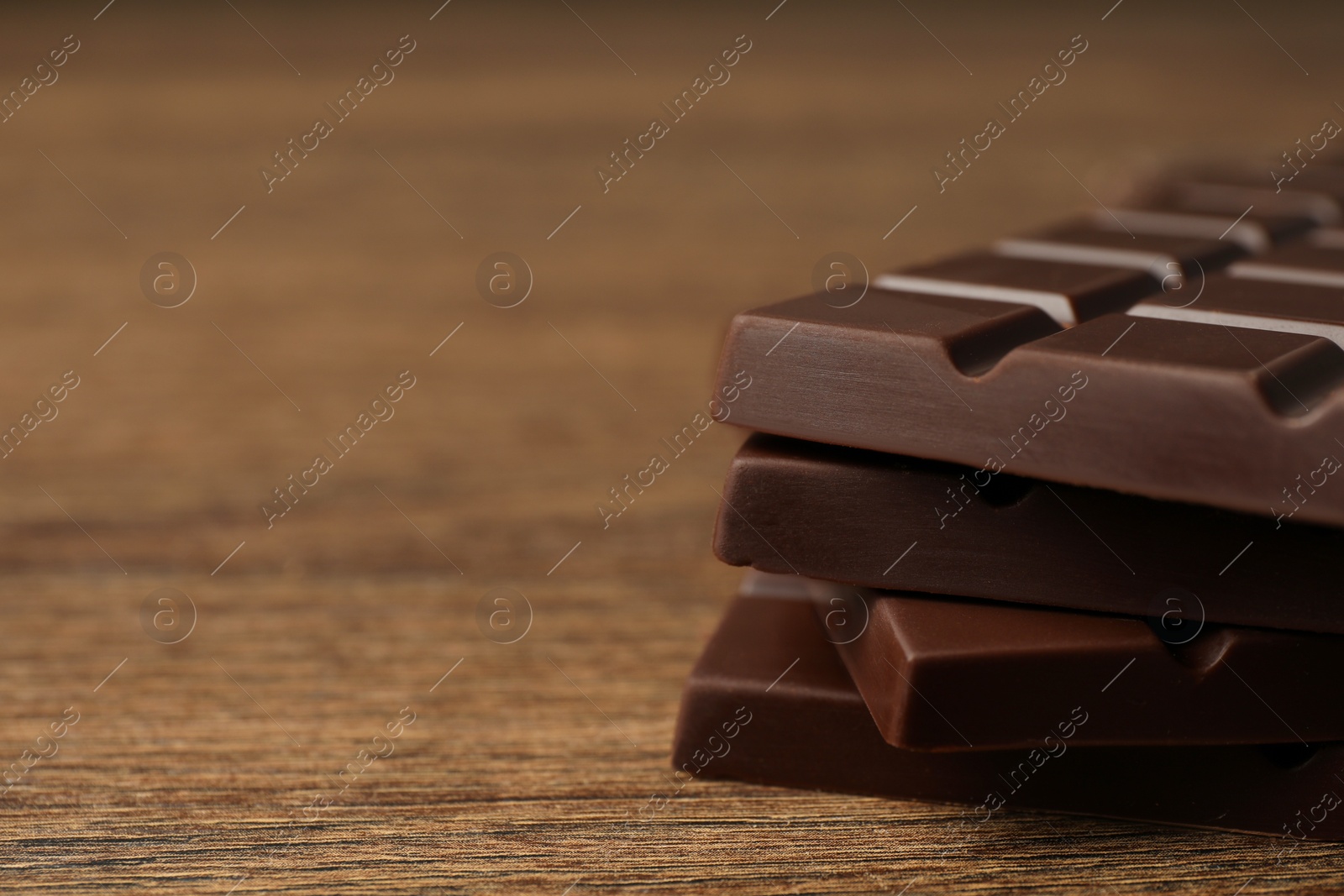 Photo of Pieces of tasty chocolate bars on wooden table, closeup. Space for text