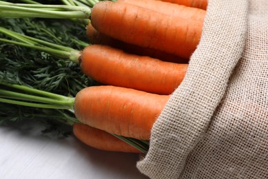 Sack with tasty ripe carrots on white wooden table, closeup