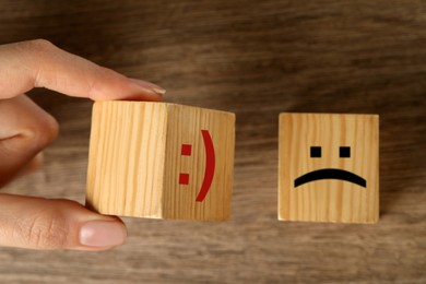 Image of Woman choosing cube with happy face instead of another one with sad at wooden table, top view