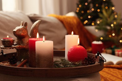 Photo of Tray with beautiful burning candles and Christmas decor on sofa at home