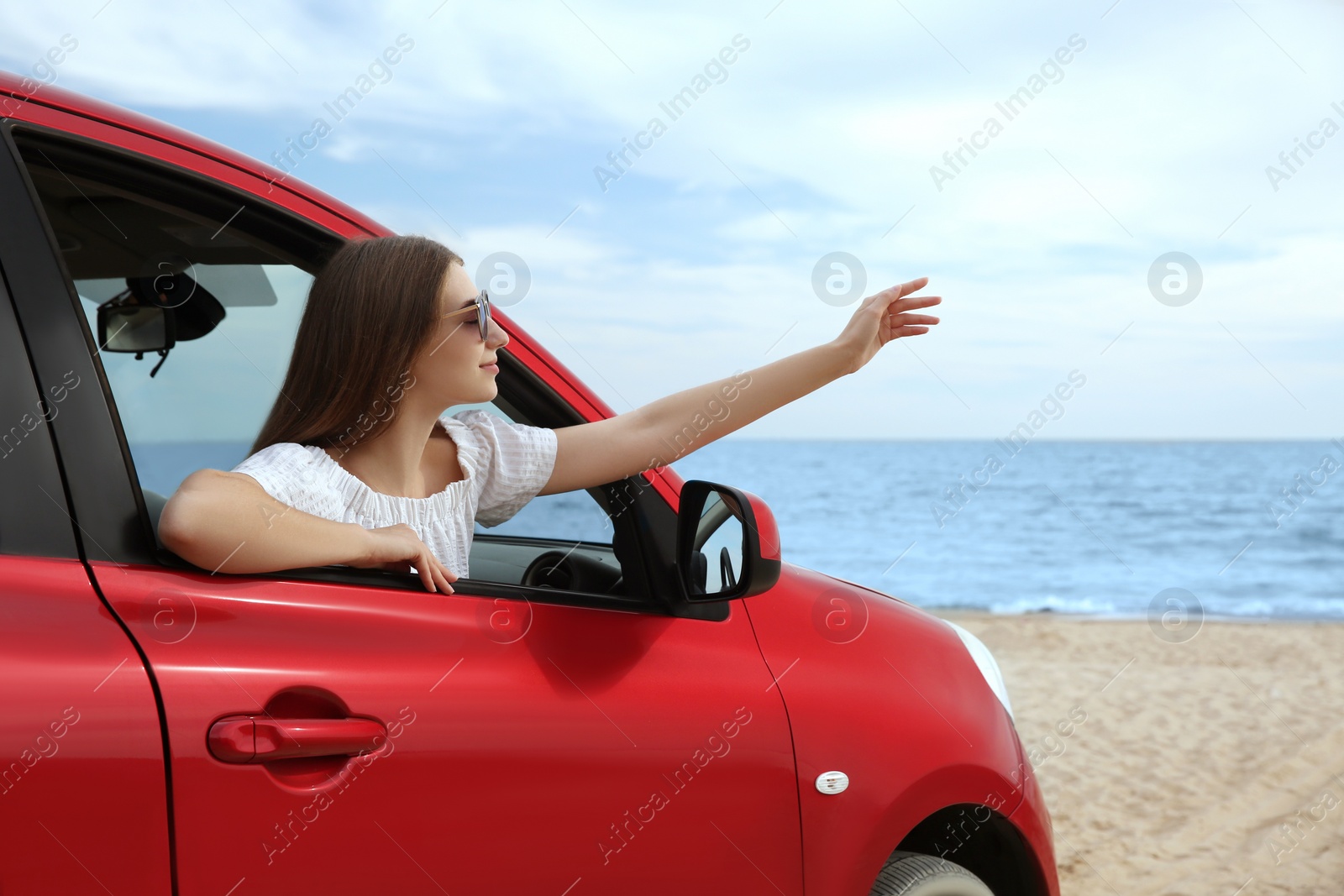 Photo of Happy woman leaning out of car window on beach. Summer vacation trip