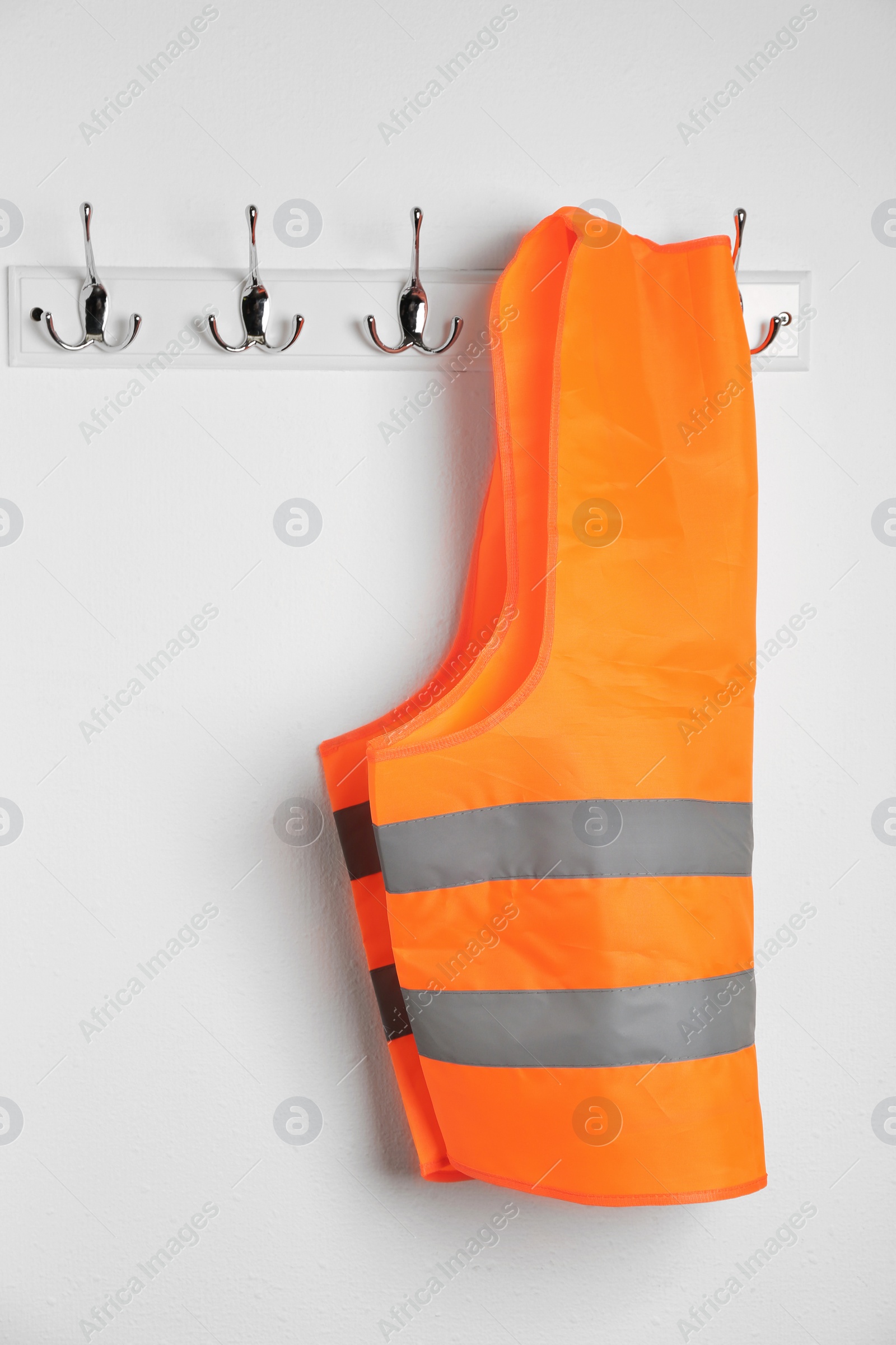 Photo of Reflective vest hanging on white wall. Safety equipment