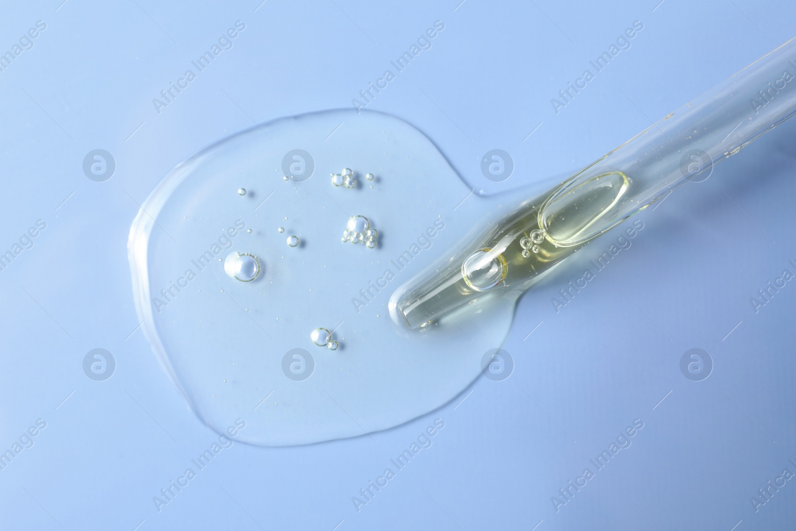 Photo of Dripping hydrophilic oil from pipette on light blue background, top view