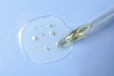 Photo of Dripping hydrophilic oil from pipette on light blue background, top view