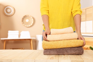 Woman stacking clean towels on wooden table in laundry room, closeup. Space for text