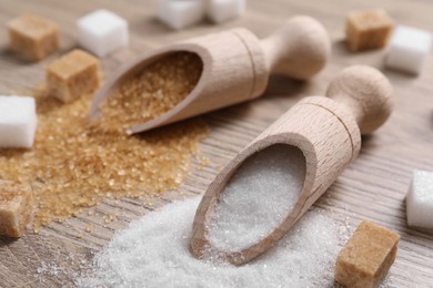 Photo of Scoops with different types of sugar on wooden table, closeup