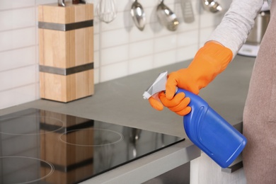 Photo of Woman cleaning stove with detergent in kitchen, closeup