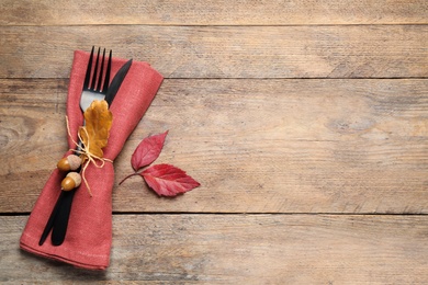 Photo of Top view of cutlery with acorns, autumn leaves and napkin on wooden table, space for text. Thanksgiving Day
