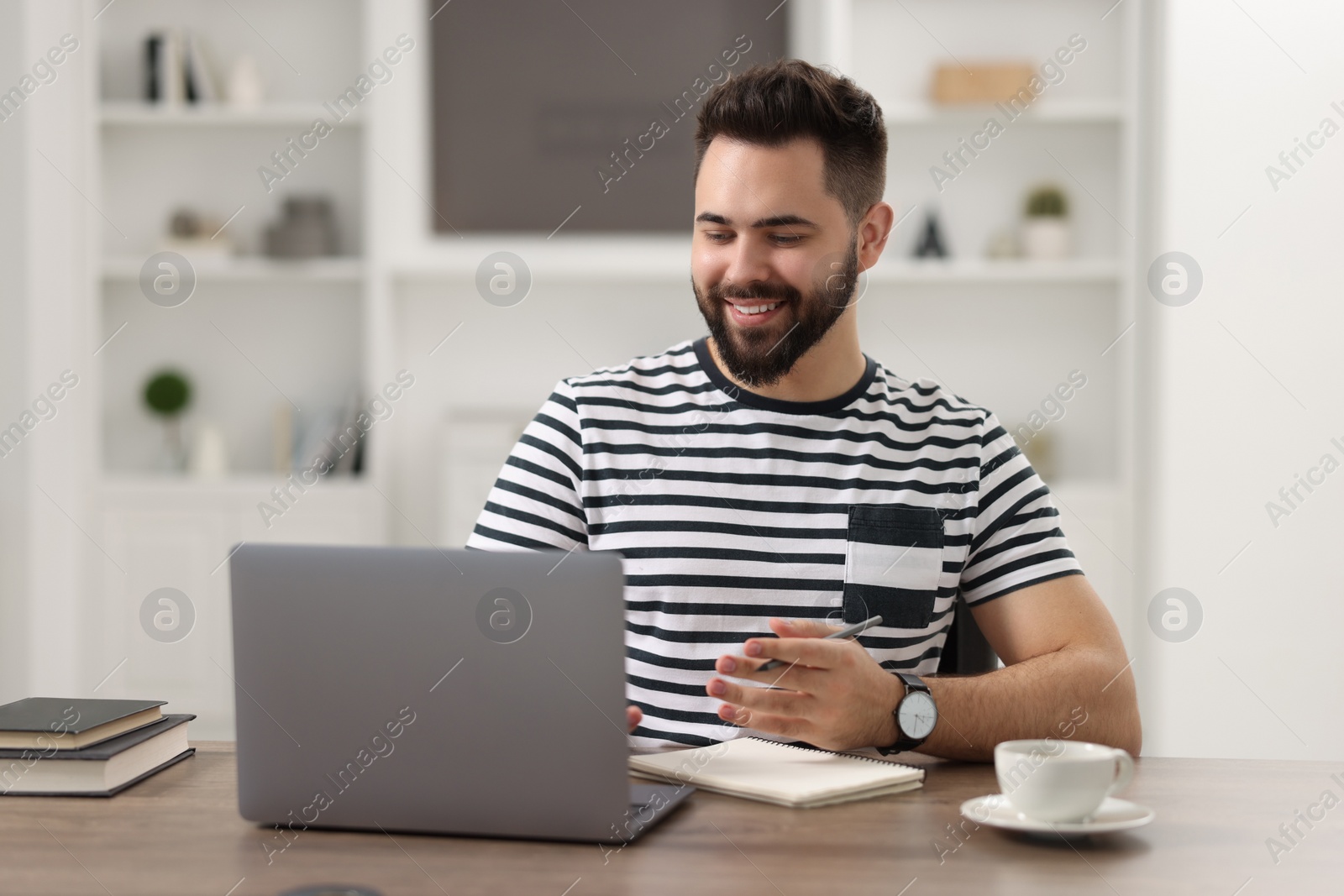 Photo of Young man watching webinar at table in room