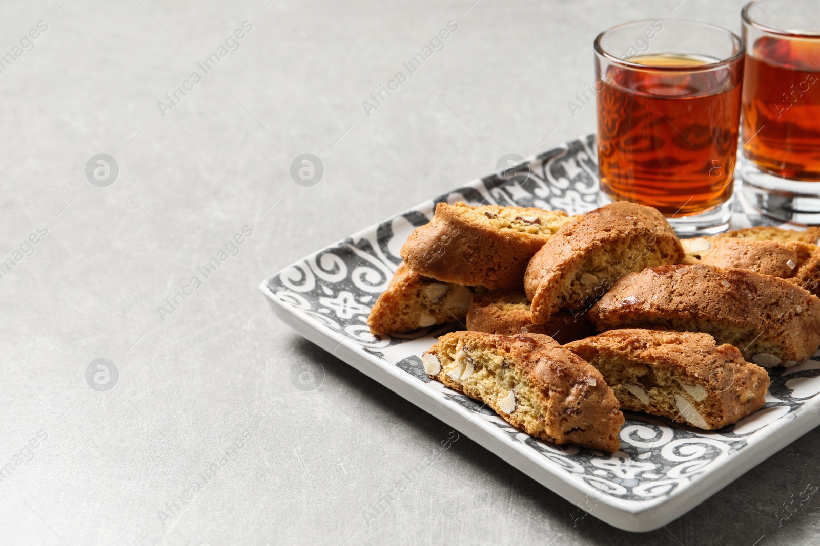 Photo of Tray with tasty cantucci and glasses of liqueur on light table, space for text. Traditional Italian almond biscuits