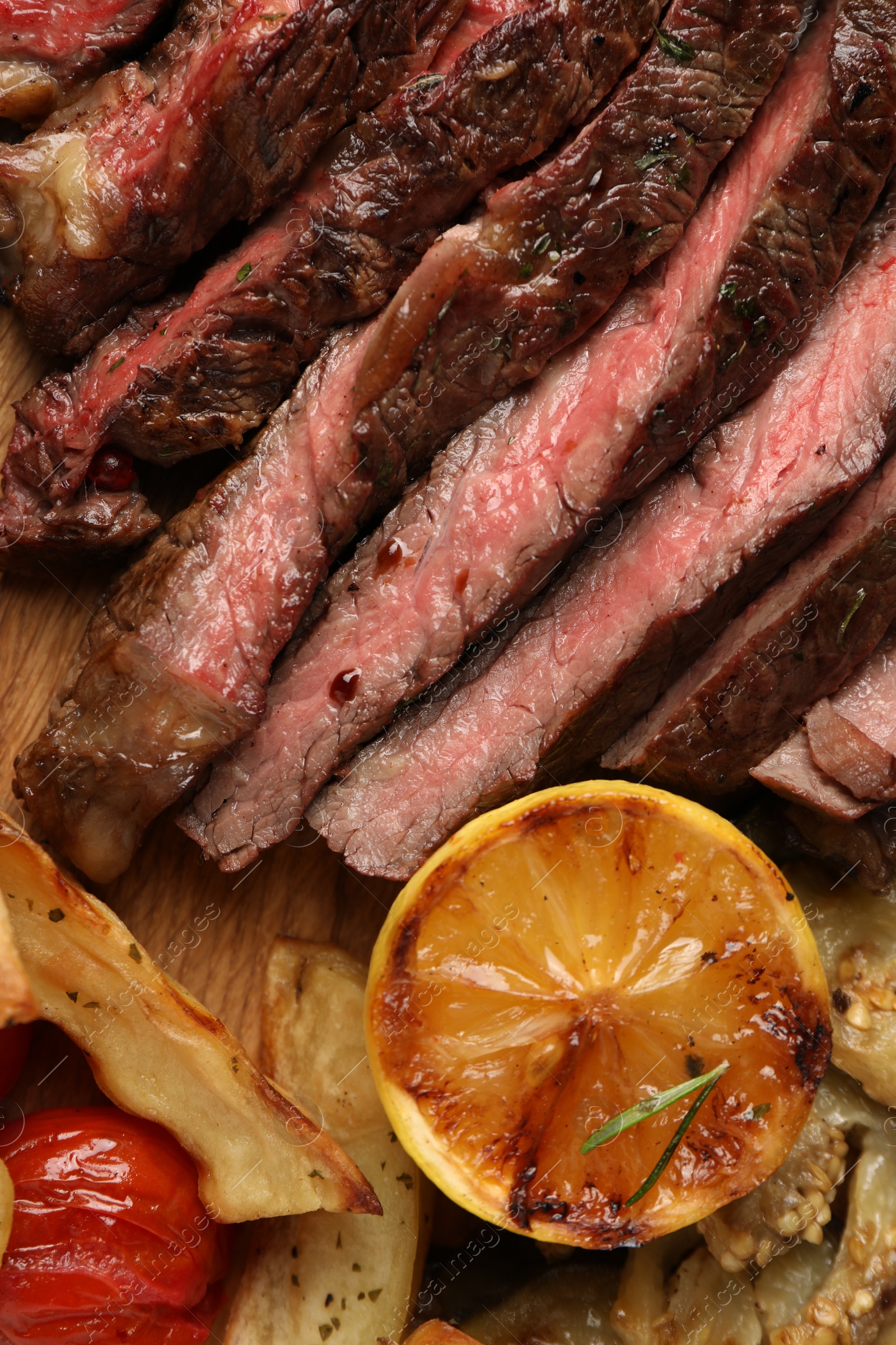 Photo of Delicious grilled beef with vegetables, lemon and spices on table, top view