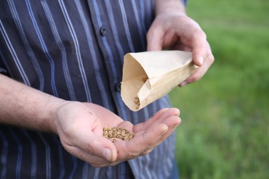 Photo of Man pouring beet seeds from paper bag into hand outdoors, closeup