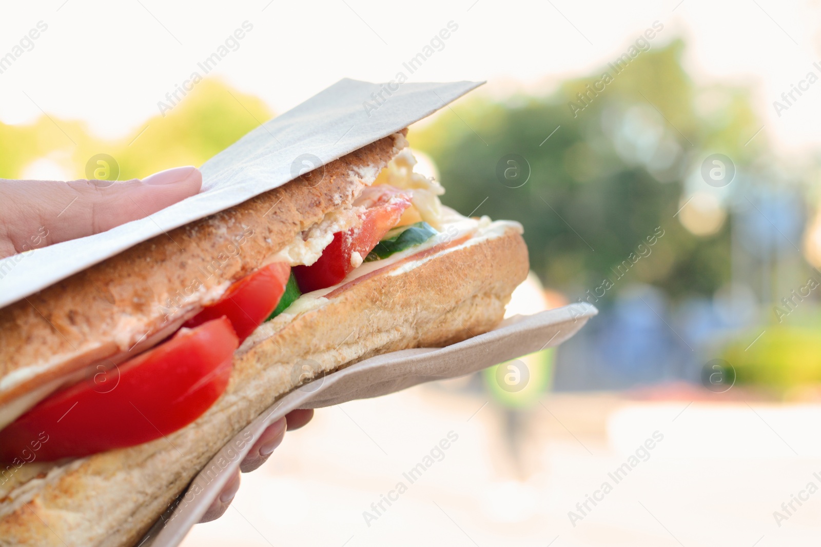 Photo of Woman holding tasty sandwich with vegetables outdoors, closeup and space for text. Street food