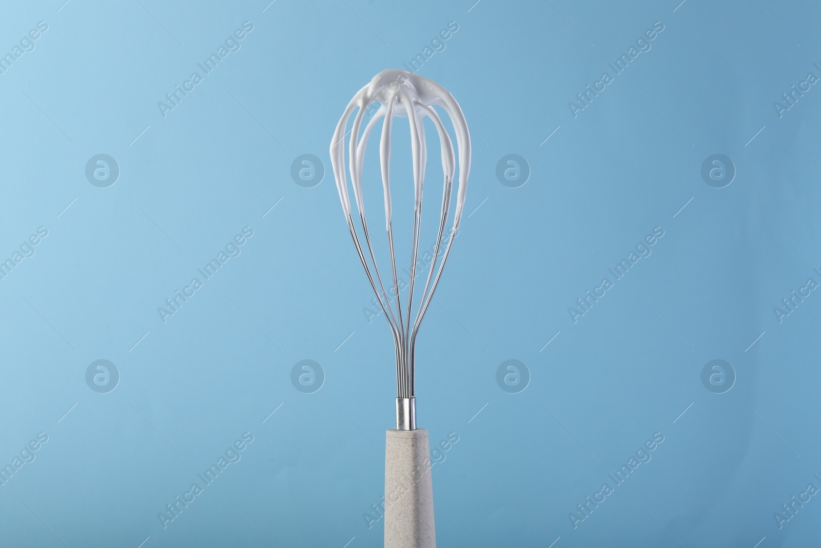 Photo of Whisk with whipped cream on light blue background