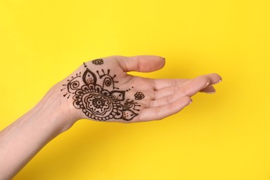 Photo of Woman with henna tattoo on palm against yellow background, closeup. Traditional mehndi ornament