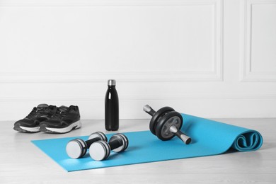 Exercise mat, dumbbells, ab roller, shoes and bottle of water on light wooden floor indoors