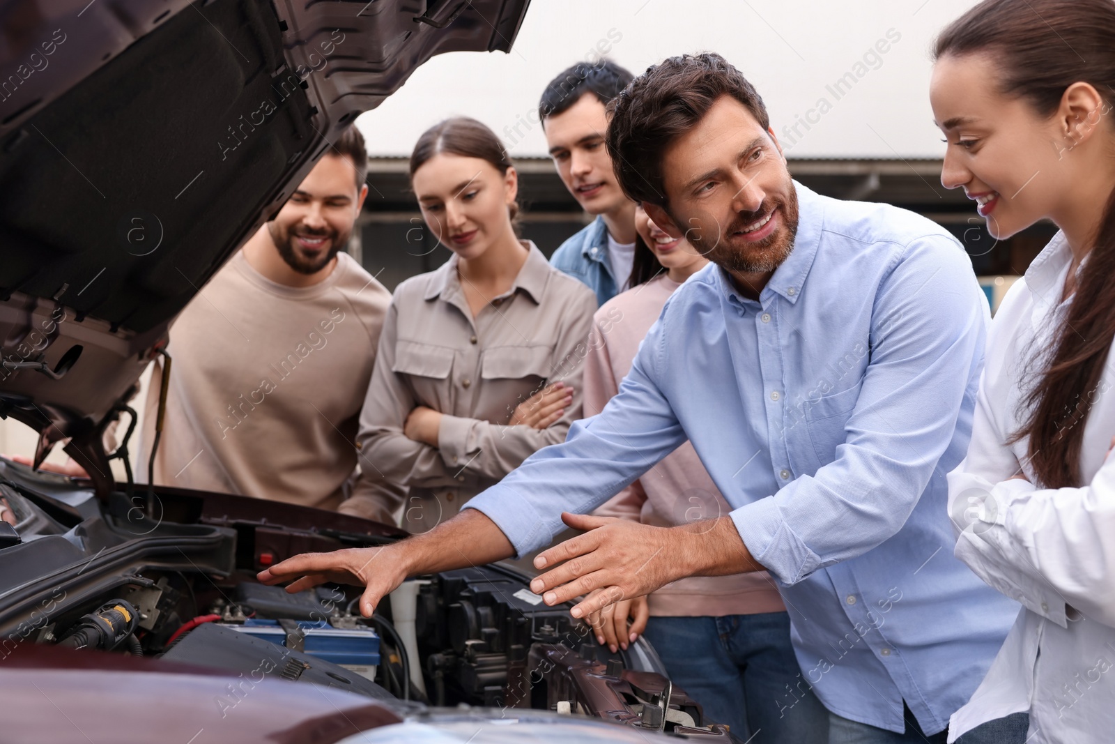 Photo of Driving school. Teacher explaining car engine to group outdoors