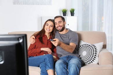 Photo of Happy young couple watching TV on sofa at home