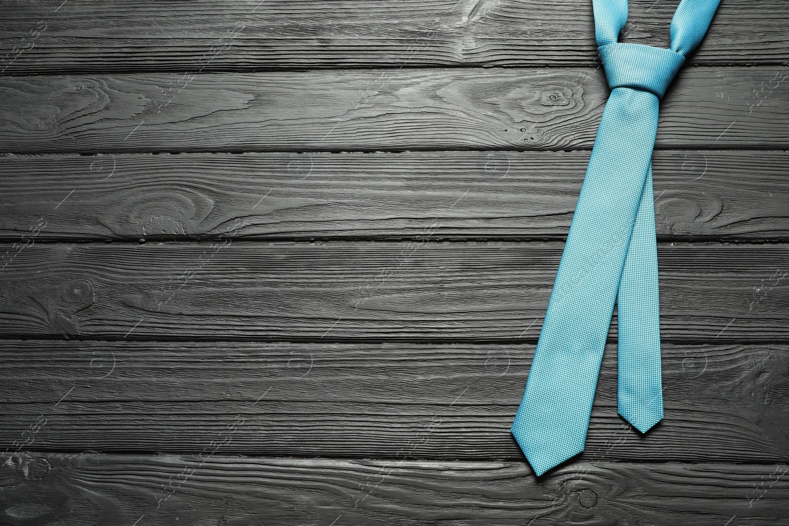 Photo of One light blue necktie on black wooden table, top view. Space for text