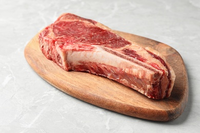 Wooden board with raw beef meat on light grey marble table, closeup