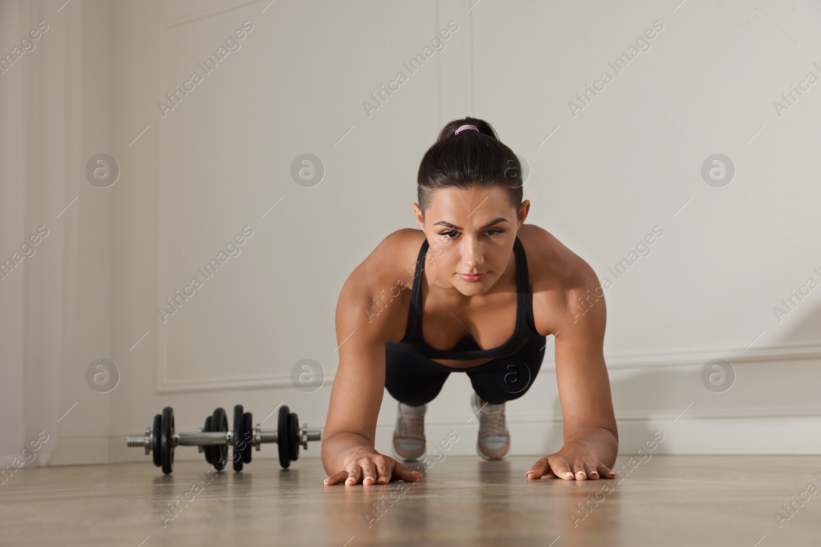 Photo of Young woman doing plank exercise on floor indoors