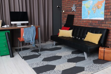 Stylish teenager's room with computer, black sofa and world map on brick wall