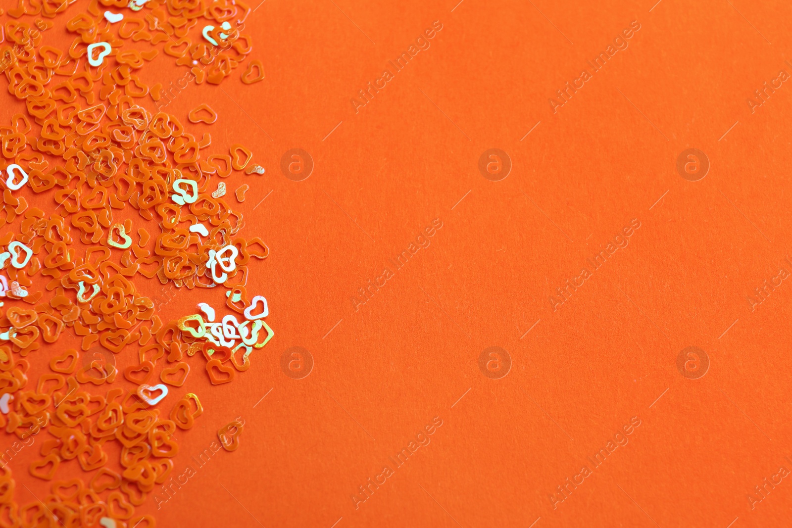 Photo of Shiny bright heart shaped glitter on coral background. Space for text