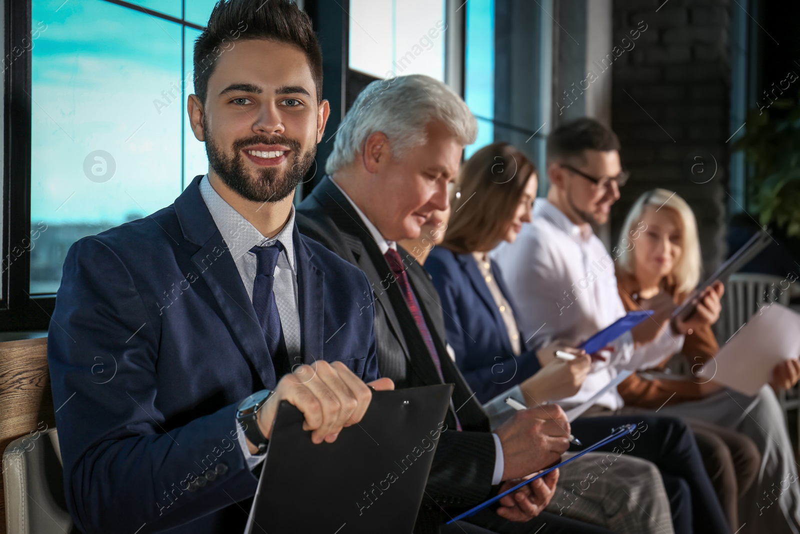 Photo of Young man with clipboard waiting for job interview in office hall
