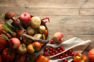 Basket with different fresh ripe vegetables and fruits on wooden table, flat lay. Space for text