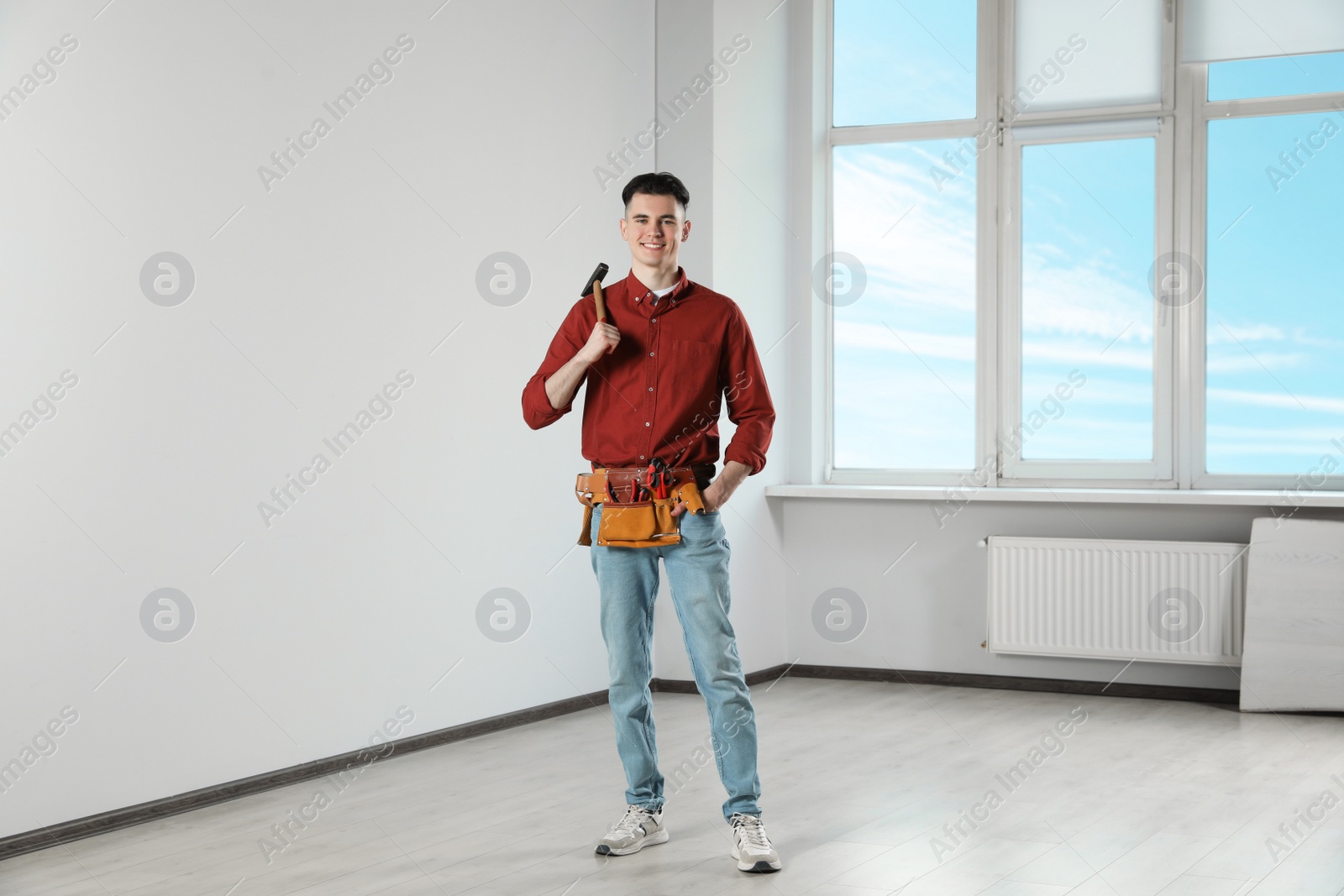 Photo of Handyman with tool belt and hammer in empty room