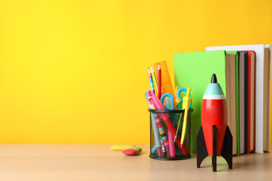 Photo of Bright toy rocket and school supplies on wooden table. Space for text