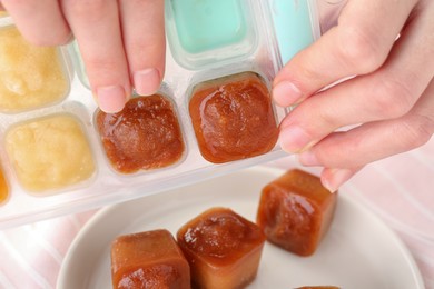 Woman taking frozen fruit puree cubes out from ice tray, closeup