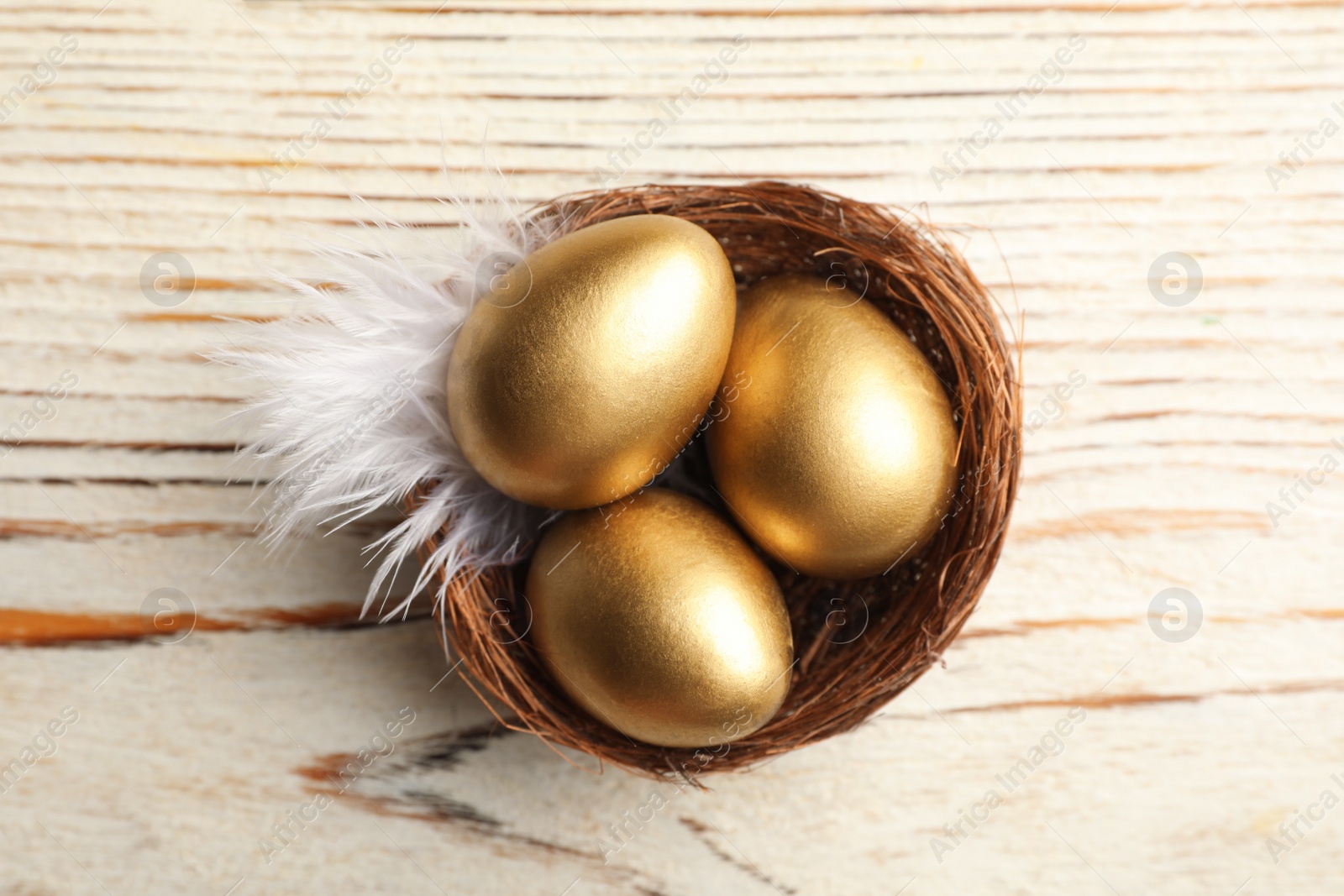 Photo of Nest with golden eggs on white wooden table, top view