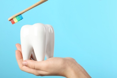 Photo of Dentist holding ceramic model of tooth and wooden brush on color background, space for text