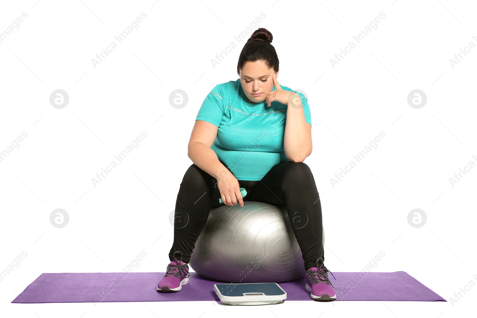 Photo of Upset overweight woman with scale, measuring tape and fitness ball on white background