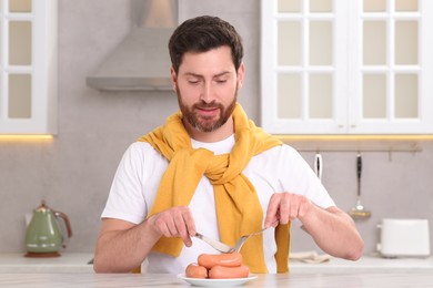 Photo of Man cutting sausages with knife at table in kitchen