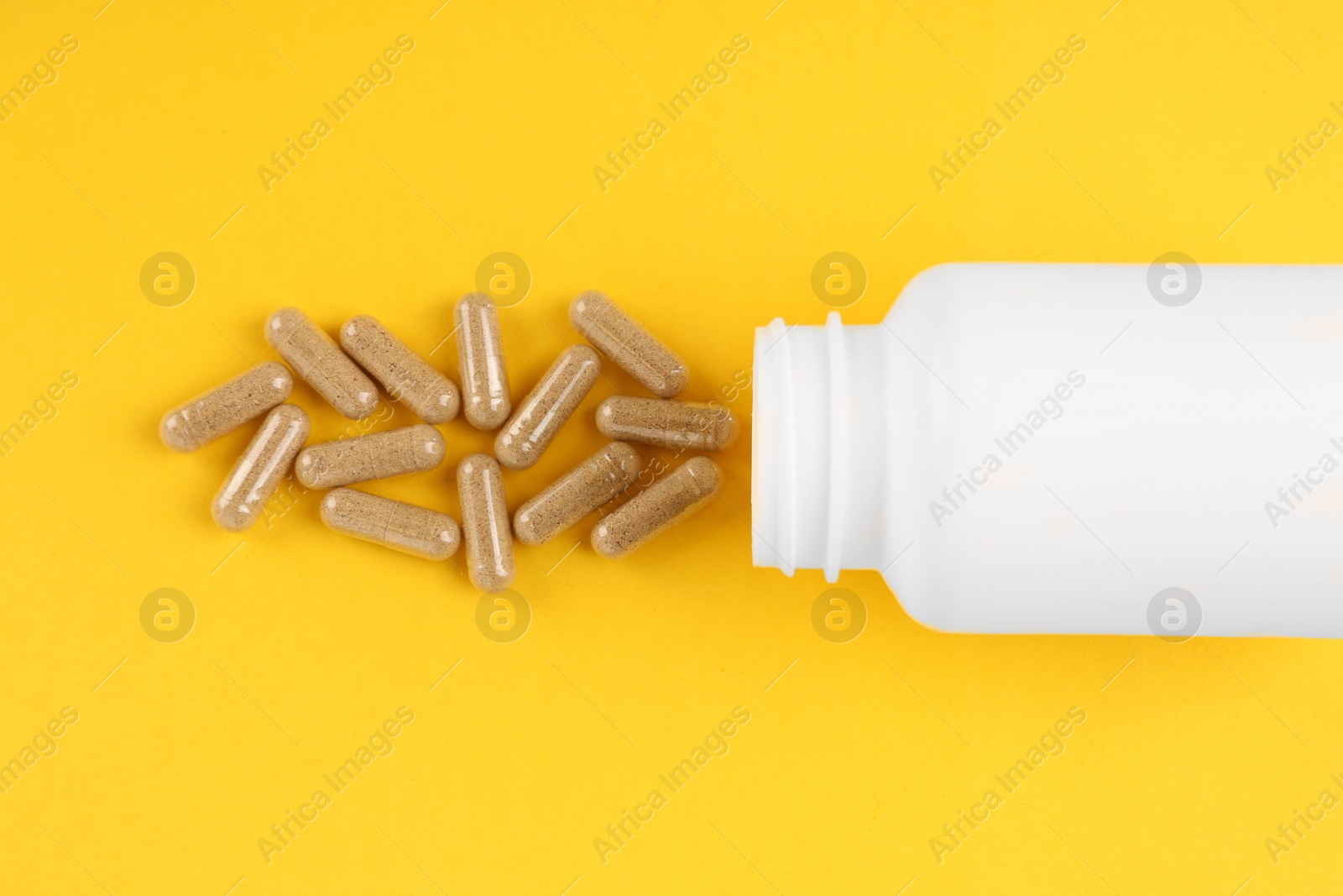 Photo of White medical bottle and vitamin capsules on yellow background, top view