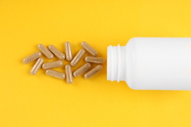 Photo of White medical bottle and vitamin capsules on yellow background, top view