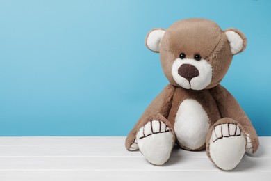Cute teddy bear on white wooden table against light blue background, space for text