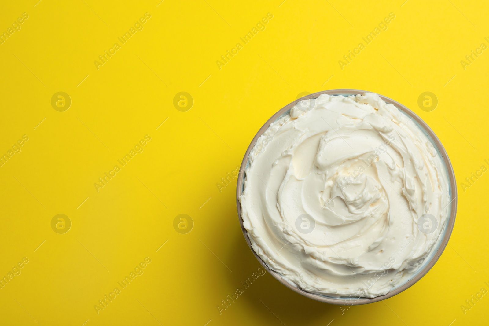 Photo of Bowl of tasty cream cheese on yellow background, top view. Space for text