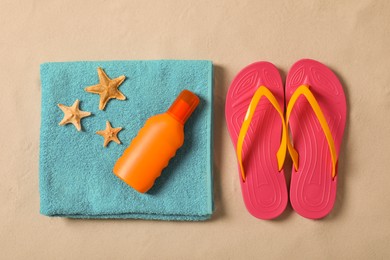 Photo of Beach towel, sunscreen, starfishes and flip flops on sand, flat lay