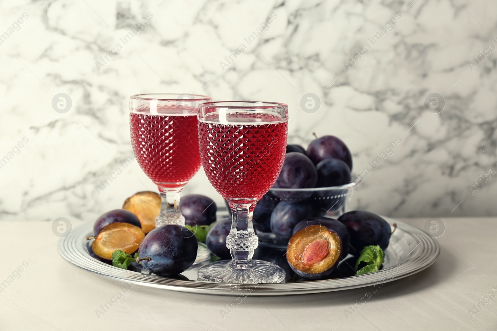 Photo of Delicious plum liquor, mint and ripe fruits on white table. Homemade strong alcoholic beverage