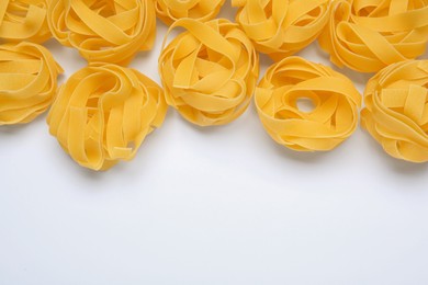 Photo of Raw tagliatelle pasta on white background, top view. Space for text