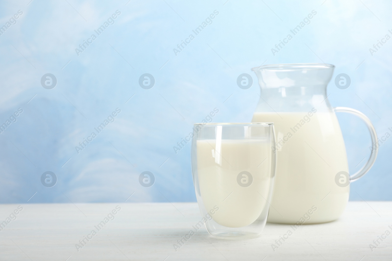 Photo of Glass and jug of fresh milk on wooden table against color background. Space for text