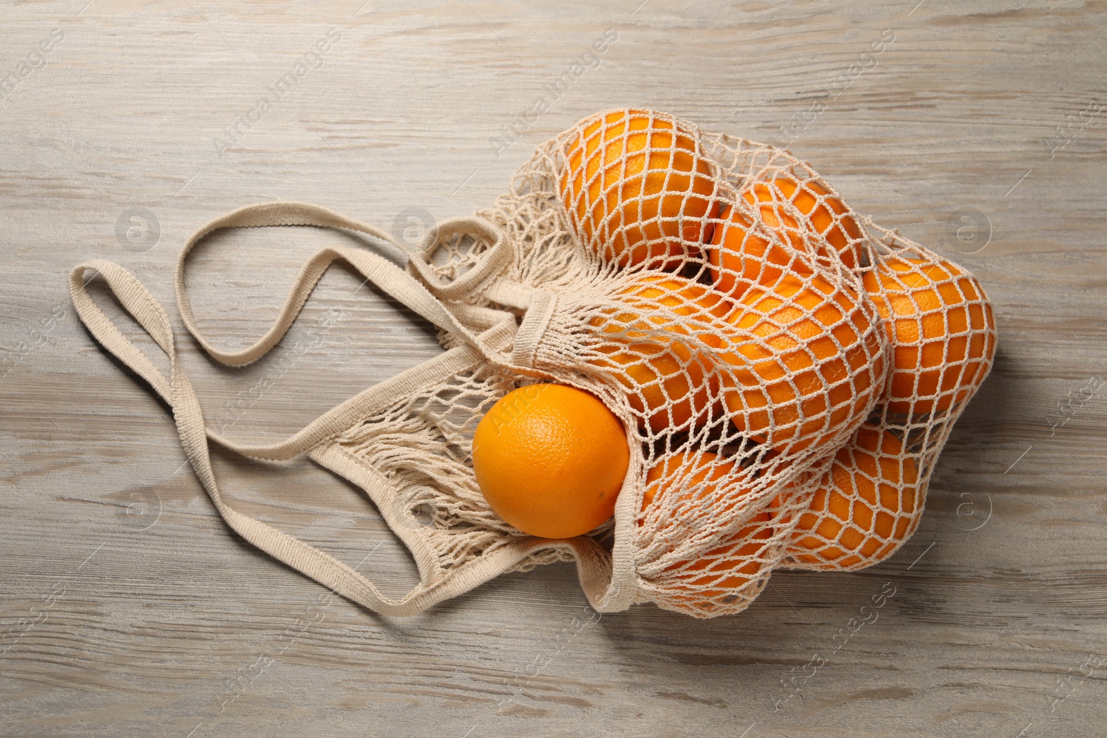 Photo of Many ripe juicy oranges with net bag on wooden table, top view