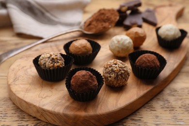 Different tasty chocolate candies on wooden board, closeup