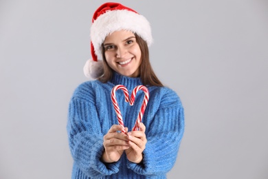 Photo of Pretty woman in Santa hat and sweater making heart with candy canes on grey background