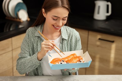 Beautiful young woman eating sushi rolls with chopsticks in kitchen