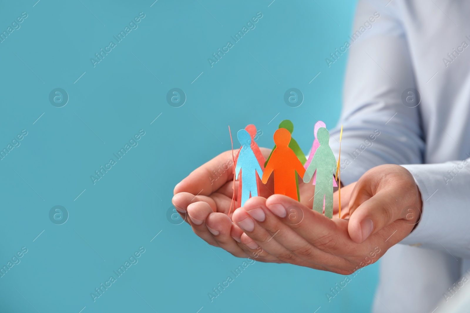 Photo of Man holding paper human figures on light blue background, closeup with space for text. Diversity and inclusion concept