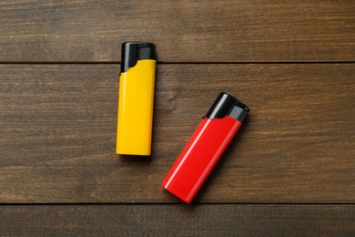 Photo of Yellow and red plastic cigarette lighters on wooden table, flat lay